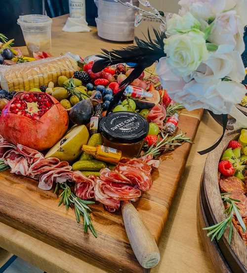 Elegant grazing board display featuring gourmet meats, cheeses, crackers, and fresh fruit, paired with delicate white florals for event catering