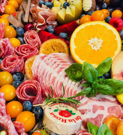Luxury charcuterie board by Rose Gold Charcuterie in Southern California featuring cured meats, blueberries, golden tomatoes, cheese, orange slices, and fresh herbs.