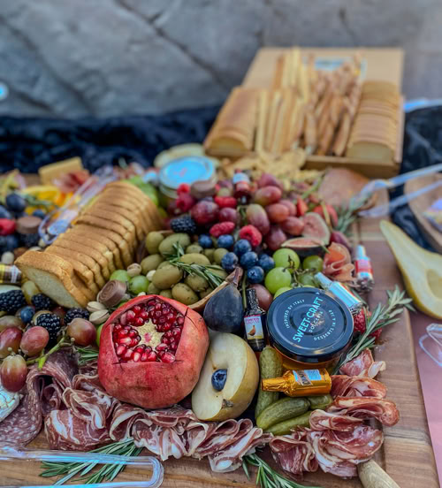 Gourmet charcuterie board with pomegranate, crackers, grapes, olives, deli meats, and artisan cheese by Rose Gold Charcuterie in glendora, ca