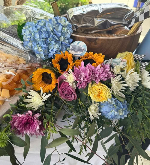 Floral arrangement with sunflowers, hydrangeas, roses, mums, greenery, and football-themed decorations on an event table.