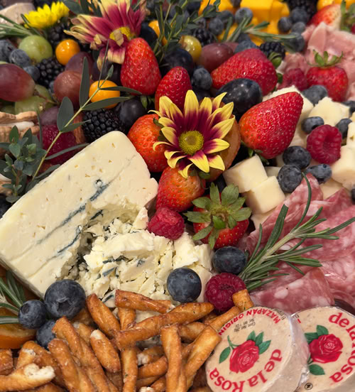 A beautifully arranged platter of various foods including fresh strawberries, grapes, and an assortment of cheeses, presented indoors on a table. The vibrant colors and textures highlight the natural appeal of the fruits and dairy products, showcasing a diverse selection for a meal or snack.