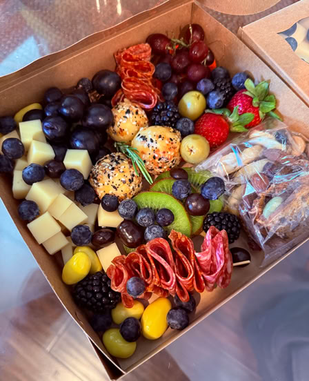 Charcuterie box with cheese cubes, salami, grapes, blueberries, blackberries, strawberries, olives, sliced apples, seasoned pastry bites, and cookies.