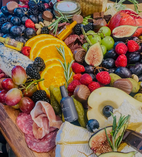 Colorful grazing table packed with orange slices, berries, cheese, chocolate, cured meats, figs, and fresh herbs by Rose Gold Charcuterie.