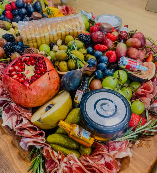 Large charcuterie board with pomegranate, figs, assorted grapes, deli meats, cheeses, pickles, and crackers by Rose Gold Charcuterie in Southern California.