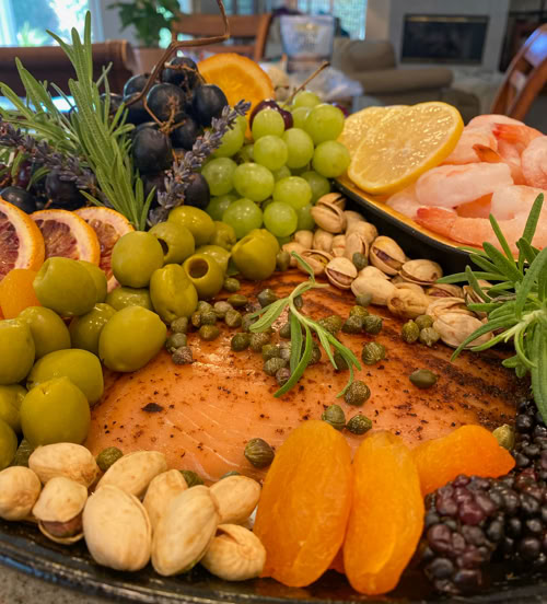 Close-up of a custom seafood charcuterie board in San Dimas, CA with shrimp, smoked salmon, olives, pistachios, fresh fruit, and herbs