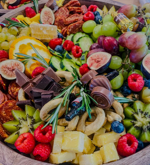 Round charcuterie board filled with kiwi, figs, citrus, crackers, chocolate, grapes, and artisan meats by Rose Gold Charcuterie in Southern California.