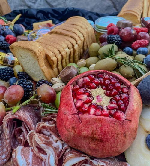 Rose Gold Charcuterie grazing board featuring a halved pomegranate, artisan crackers, cured meats, olives, berries, grapes, and gourmet cheeses—perfect for elevated entertaining and luxury catering.