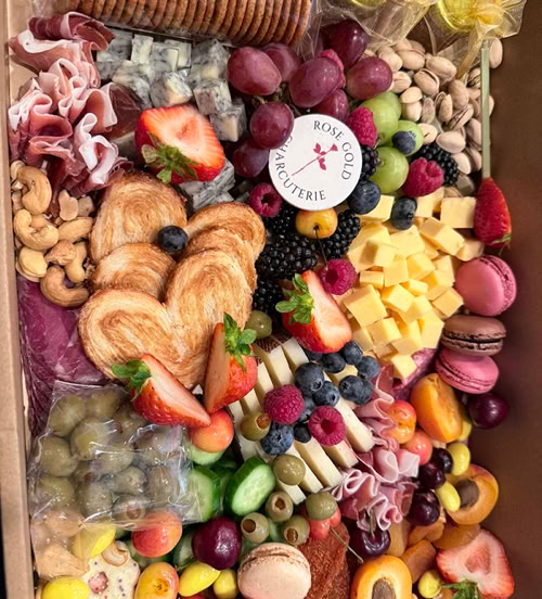 Large charcuterie box filled with crackers, cheeses, cured meats, fresh berries, grapes, olives, nuts, macarons, pastries, and dried fruit.
