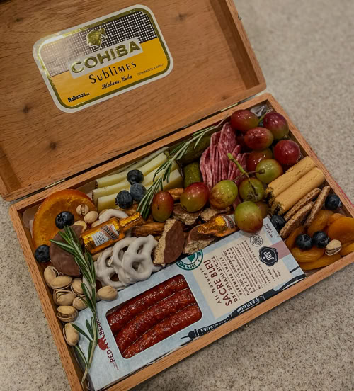 Mini charcuterie box arranged in a vintage cigar case with meats, grapes, nuts, cheese, and crackers—perfect for gifting or personal events.
