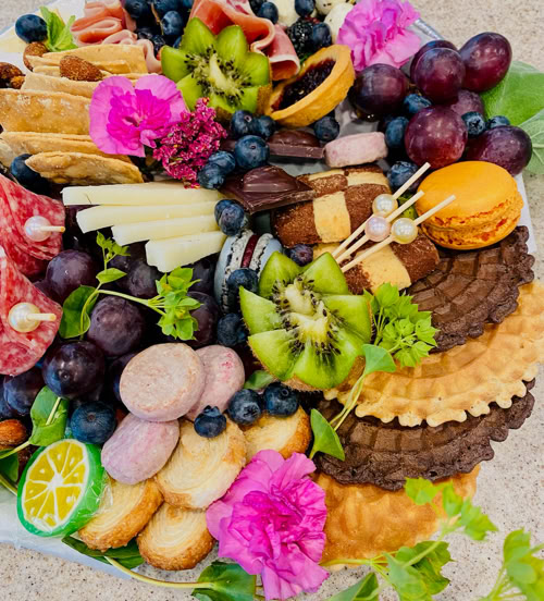 Artfully arranged charcuterie board by Rose Gold Charcuterie in Southern California featuring grapes, kiwi, cheese, meats, cookies, macarons, and edible flowers.