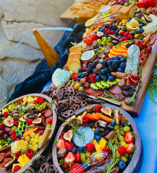 Full grazing table setup with artisan charcuterie boards, crackers, chocolate, fruits, and cheese for large events and celebrations.